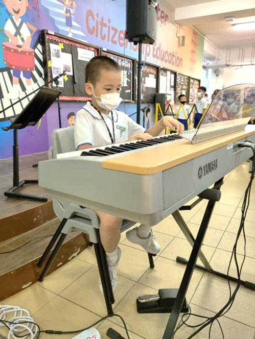 A young boy in Maha Bodhi School PE attire performing using Yamaha Keyboard in MBS Got Talents session.